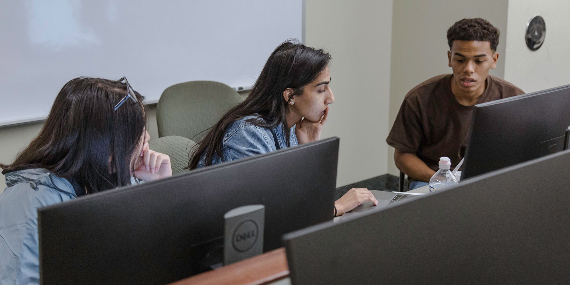 Three students at a desk behind a few computers